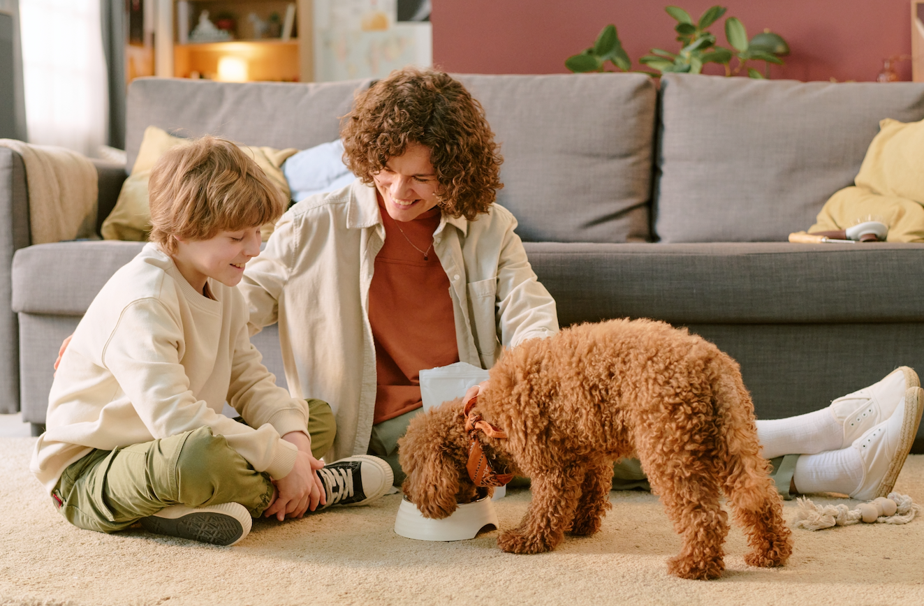 Woman and child sitting on the floor with a dog in a living room.